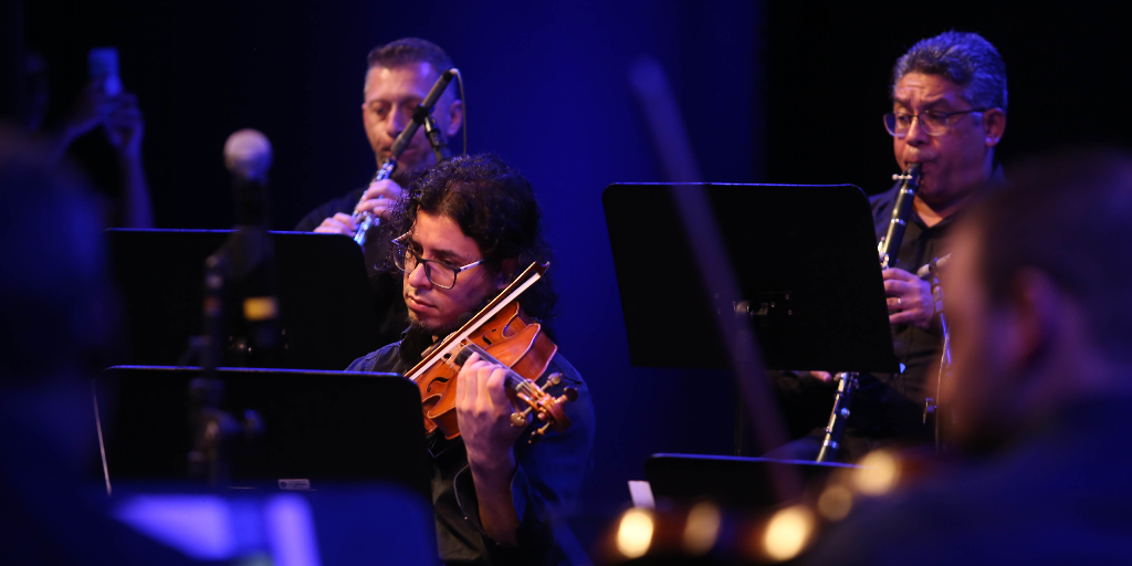 Três músicos de orquestra tocando dois instrumentos de sopro e um violino