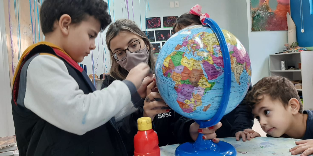 Professora, ensinando três alunos com um globo terrestre