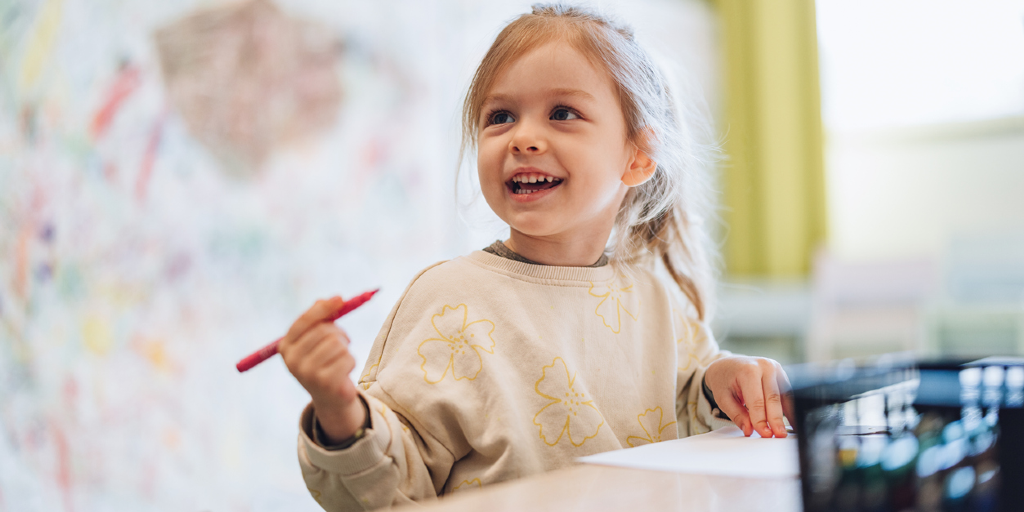Crianã pintando sobre uma mesa com giz de cera