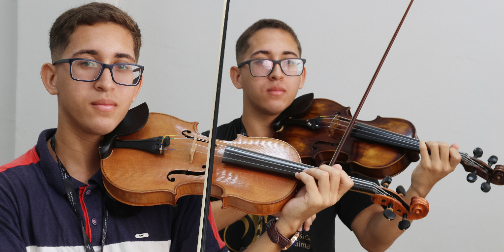 Alunos, irmãos gêmeos posam com seus violinos postados nos ombros.