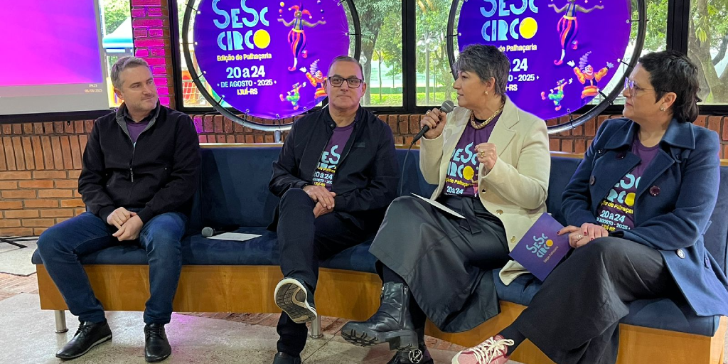 Dois homens e duas mulheres sentados conversam em frete à placa do SESC Circo