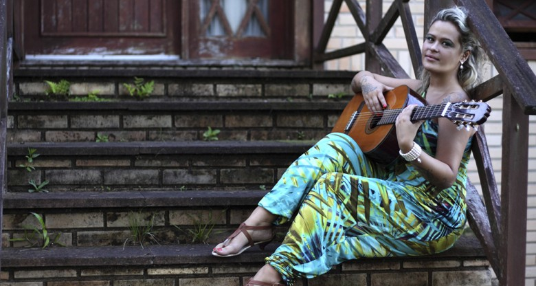 Cantora Tati Portella, sentada em uma escada tocando um violão