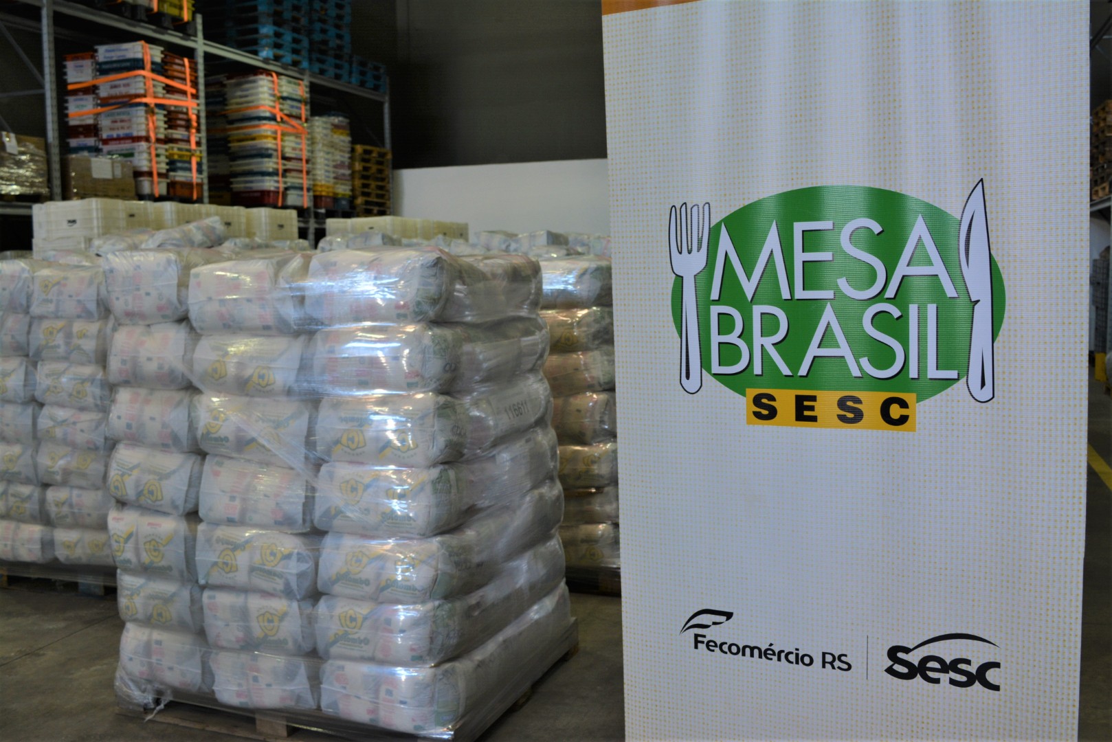 Imagem do banner do Programa Mesa Brasil Sesc ao lado das cestas básicas arrecadadas