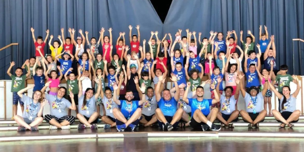 Grupo de crianças e professores com as mãos levantadas, posando para a foto
