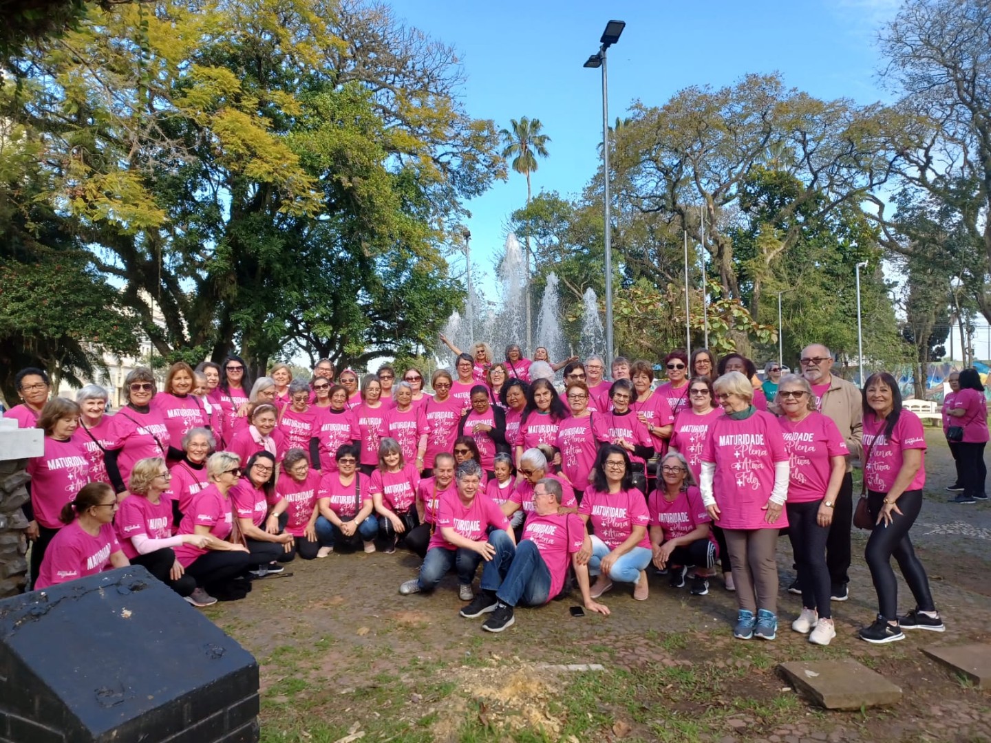 Grupo de pessoas da Maturidade Ativa do Sesc, vestidas com camiseta rosa festiva, posadas para foto ao ar livre.