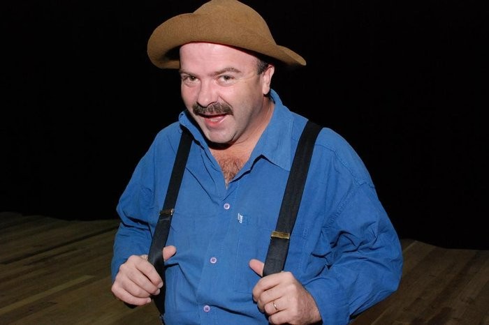 Paulinho Mixaria, comediante de chapéu e bigode, em palco fazendo apresentações.