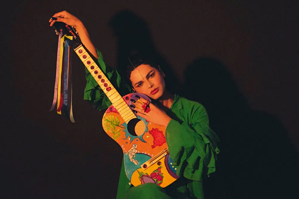 Artista Assucena abraçando um violão ornado