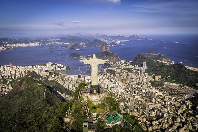 Imagem aérea do Cristo Redentor, famoso ponto turístico do Rio de Janeiro, com a praia ao fundo.