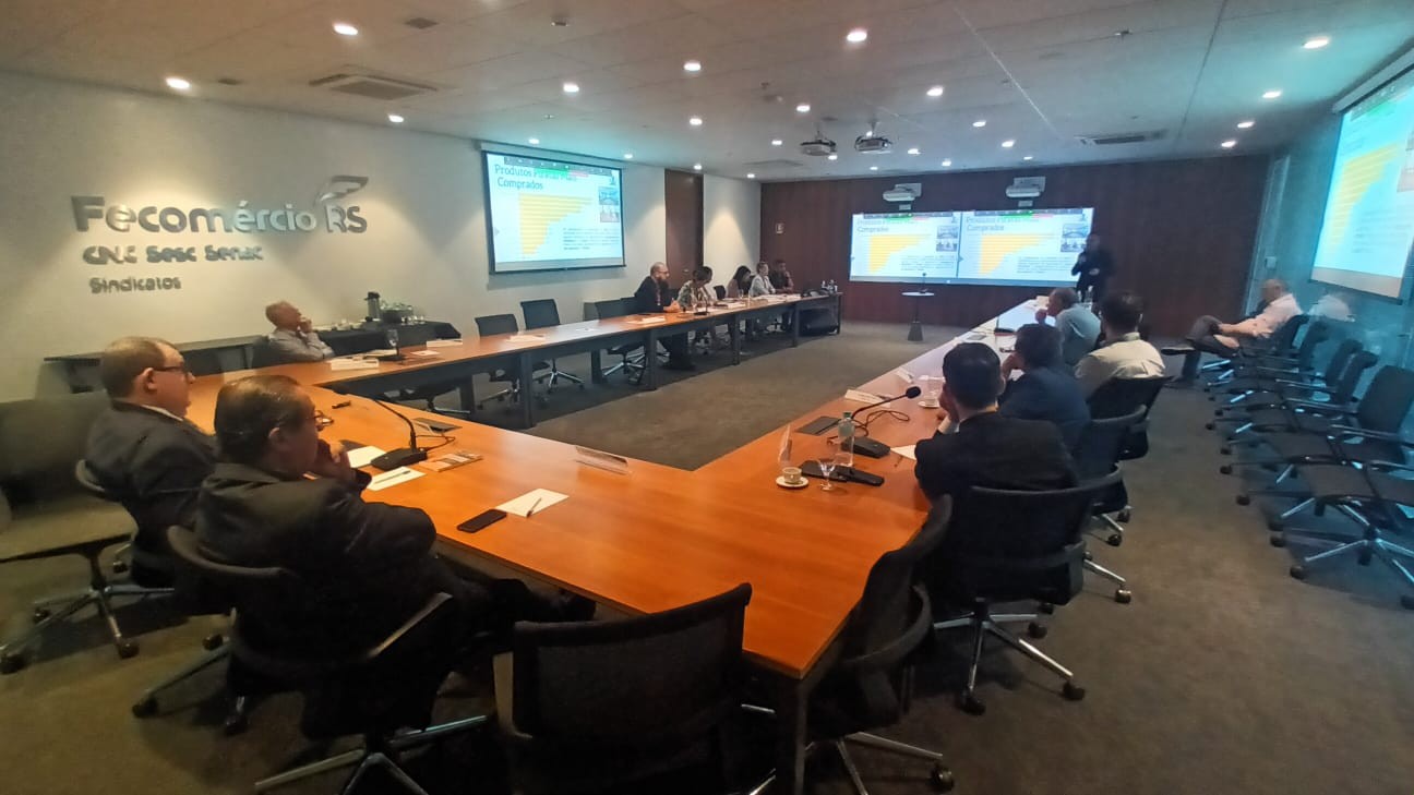 Integrantes da Comissão de Combate à Informalidade sentam-se em mesa de reunião e assistem à apresentação de slides projetados.