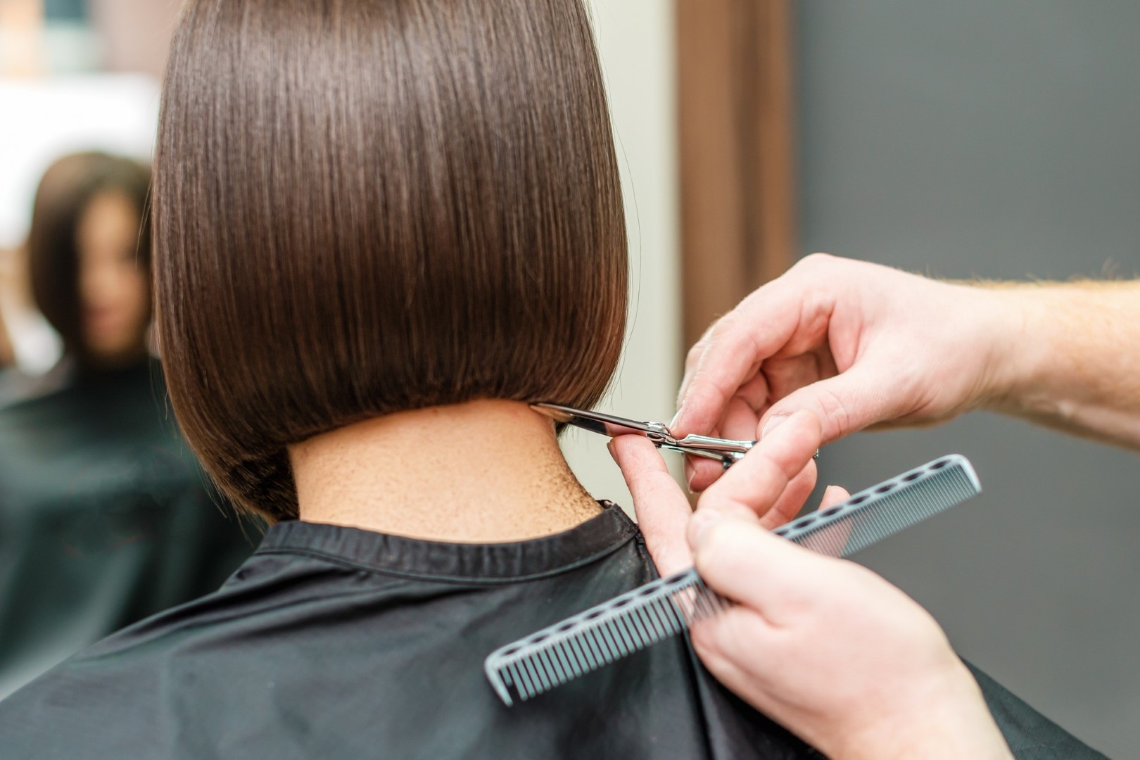 Mulher sentada em uma cadeira de salão tendo seu cabelo cortado por um homem.