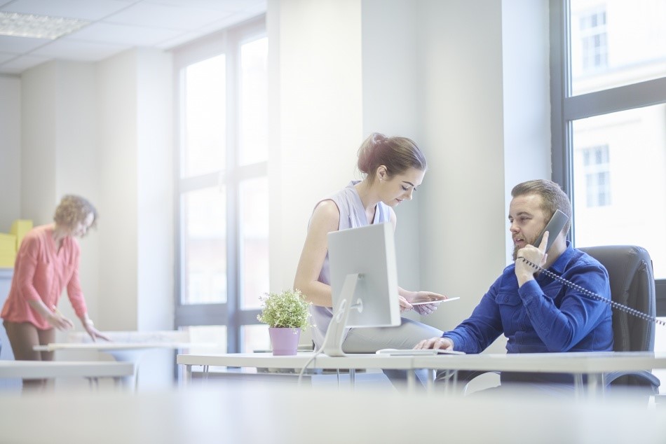 Ambiente de trabalho, homem atendendo telefone e utilizando o computador.