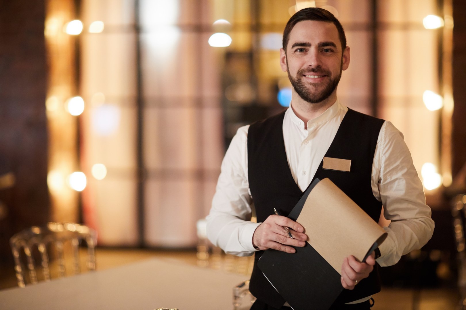 Retrato da cintura para cima de um garçom bonito sorrindo alegremente para a câmera em pé no restaurante ou café de luxo, copie o espaço